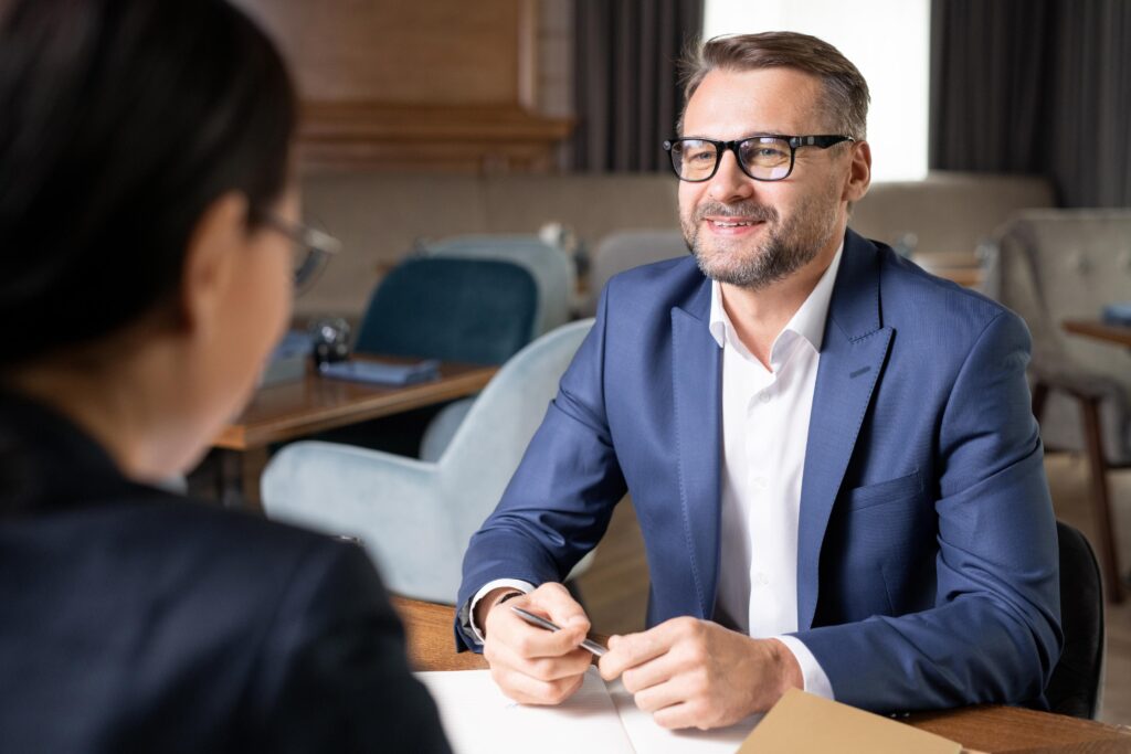 Happy confident businessman in formalwear and eyeglasses looking at colleague