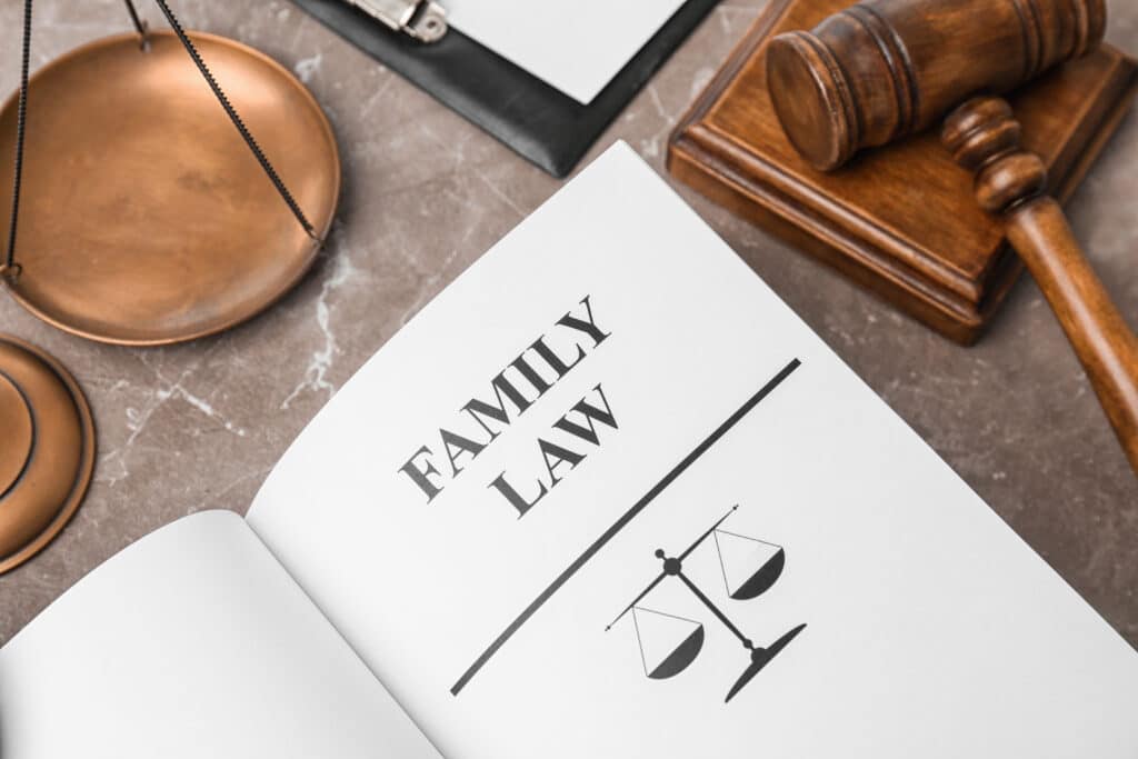 An open book displays "Family Law" next to a symbolic scale on a marble surface, with a wooden gavel and clipboard