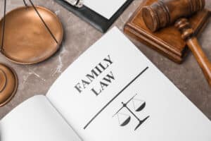 An open book displays "Family Law" next to a symbolic scale on a marble surface, with a wooden gavel and clipboard