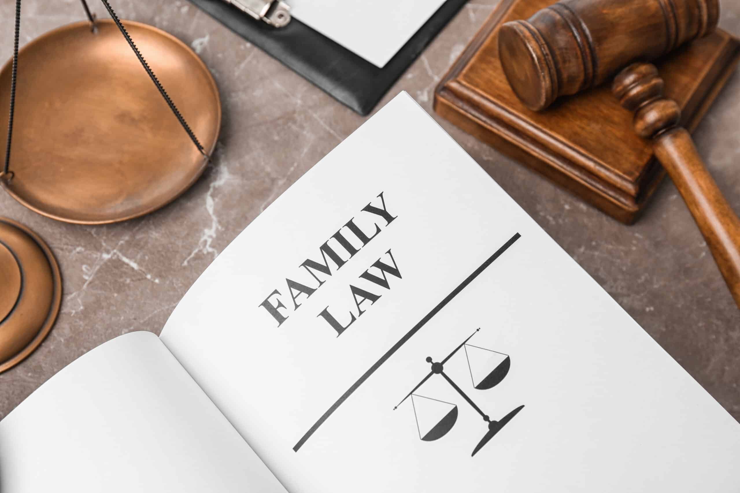 An open book displays "Family Law" next to a symbolic scale on a marble surface, with a wooden gavel and clipboard